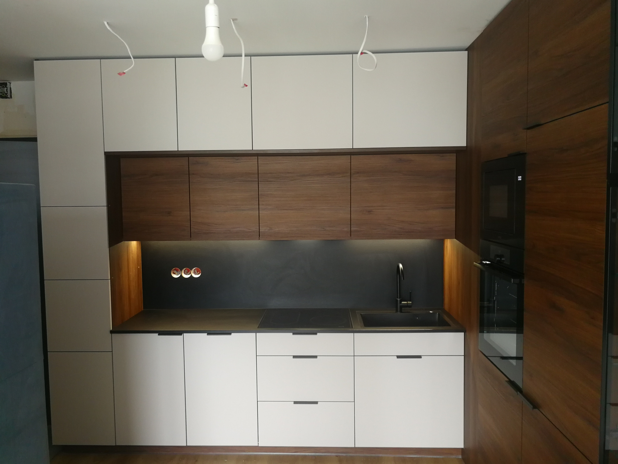 Nowoczesna kuchnia na wymiar w Gdańsku z białymi frontami i drewnianymi akcentami. Widoczne gniazdka nad blatem i minimalistyczna armatura.