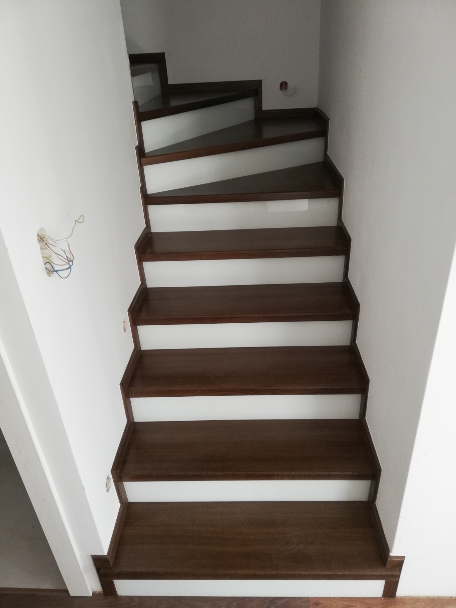 Wewnętrzne schody drewniane z białymi podstopnicami, widok z dołu, na ścianie widoczne kable elektryczne.