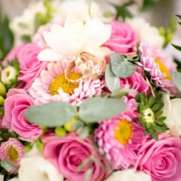 Złote obrączki ślubne spoczywają na bukiecie z różowych róż, białych tulipanów i różowych astrów z żółtymi środkami, otoczonych zielonymi liśćmi.