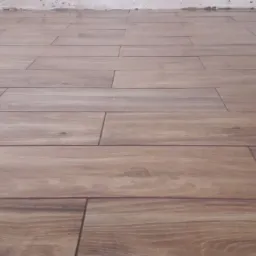 Ułożona podłoga z płytek imitujących drewno, widoczne fugi i niedokończone wykończenie ściany w tle.