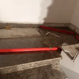 Montaż granitowych płytek na schodach wewnętrznych, widoczne poziomice, młotek i fragmenty płytek, etap prac wykończeniowych.