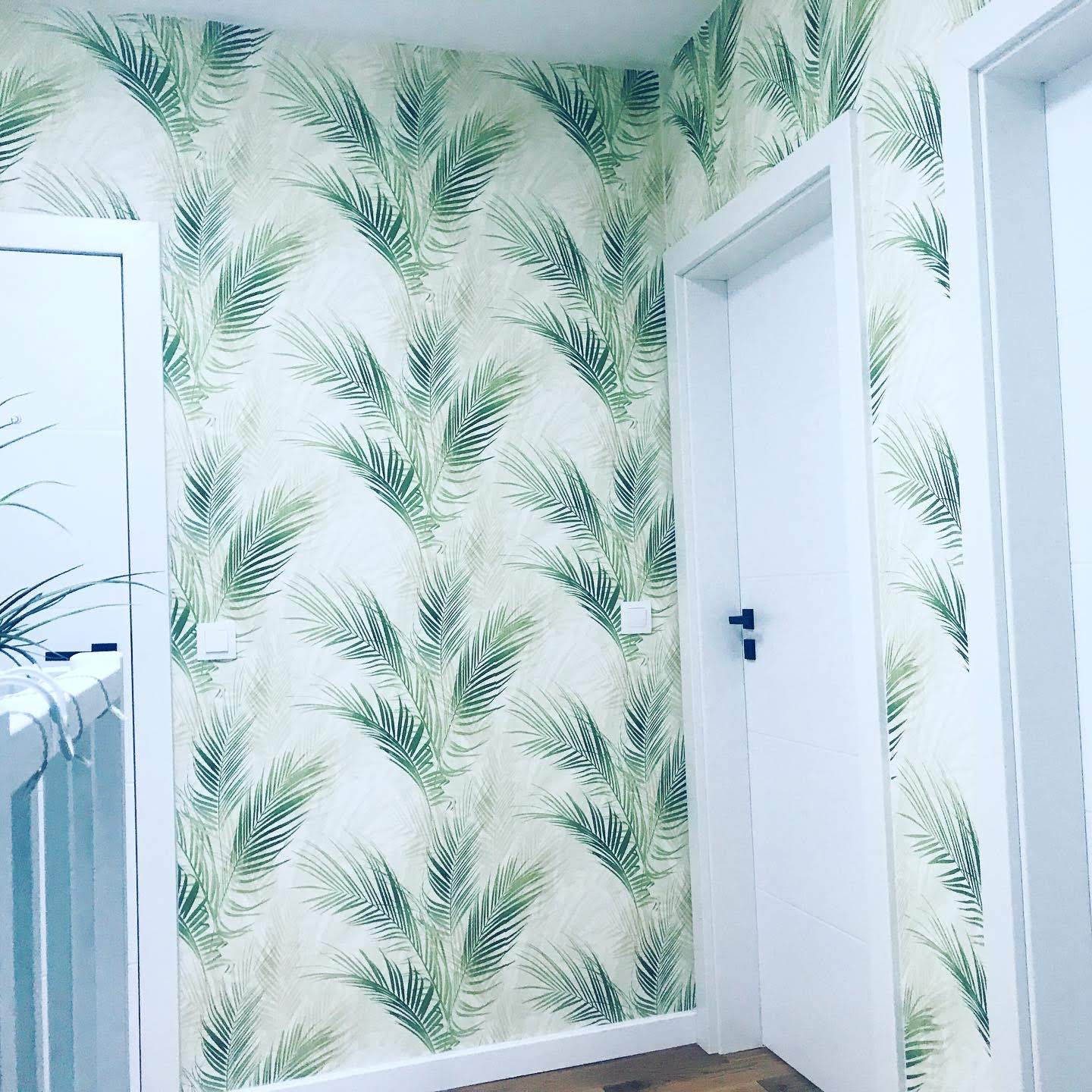 Ściana w korytarzu pokryta tapetą w motywy liści palmowych, widoczne dwie białe ościeżnice z drzwiami i drewniana podłoga.