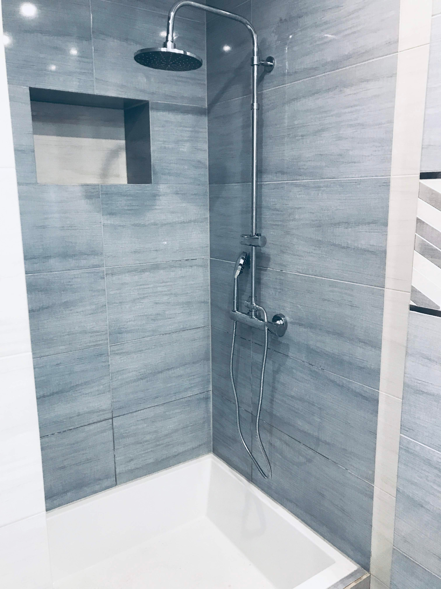 Nowoczesna kabina prysznicowa z szarymi płytkami imitującymi drewno i wnęką na kosmetyki.