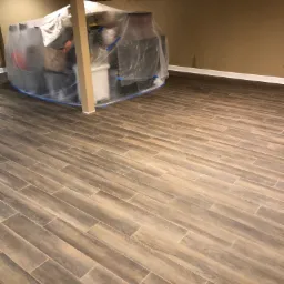 Ukończona podłoga z płytek imitujących drewno ułożonych pod kątem, zabezpieczone folią meble w tle, przygotowane do dalszych prac remontowych.