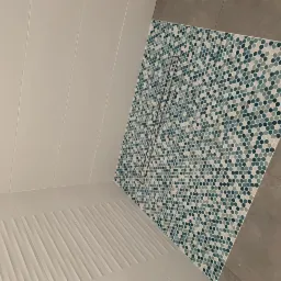 Nowoczesna kabina prysznicowa z odpływem liniowym wyłożona mozaiką w odcieniach błękitu i szarości, białe płytki ścienne i podłoga z delikatnym spadkiem w kierunku odpływu.