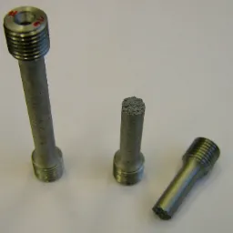 Trzy metalowe pręty z gwintem, jeden uszkodzony, leżące na jasnym tle. Pręty o różnej długości, z widoczną strukturą materiału.