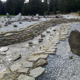 DiGarden Grzegorz Padziński - Aranżacja ogrodu z kamienną rzeczką, białym żwirem i dekoracyjnymi głazami, widok z poziomu ziemi.