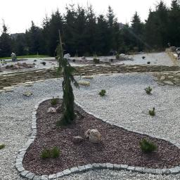 DiGarden Grzegorz Padziński - Kompozycja ogrodu z drzewkiem iglastym, kamieniami i żwirem w różnych odcieniach, obrzeże z kostki granitowej, tło z drzew iglastych.