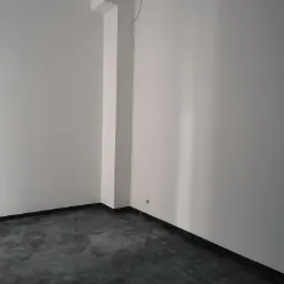 Pusty pokój z szarym, marmurkowym betonem na podłodze, świeżo pomalowane białe ściany i wystający filar z kablem zwisającym z sufitu.