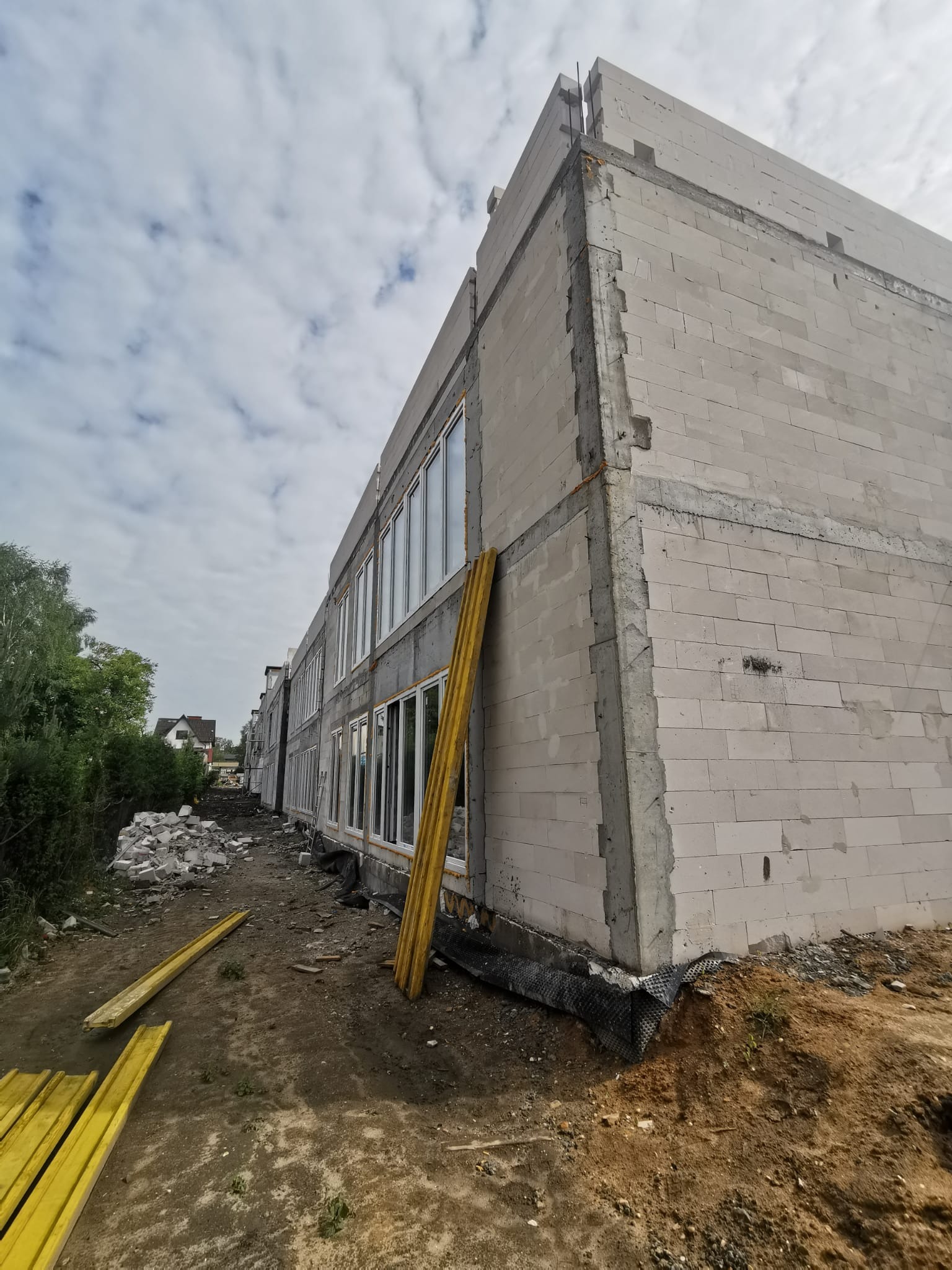 Wznoszenie ścian budynku z betonu komórkowego, widoczne okna i elementy szalunkowe, teren budowy w trakcie prac.