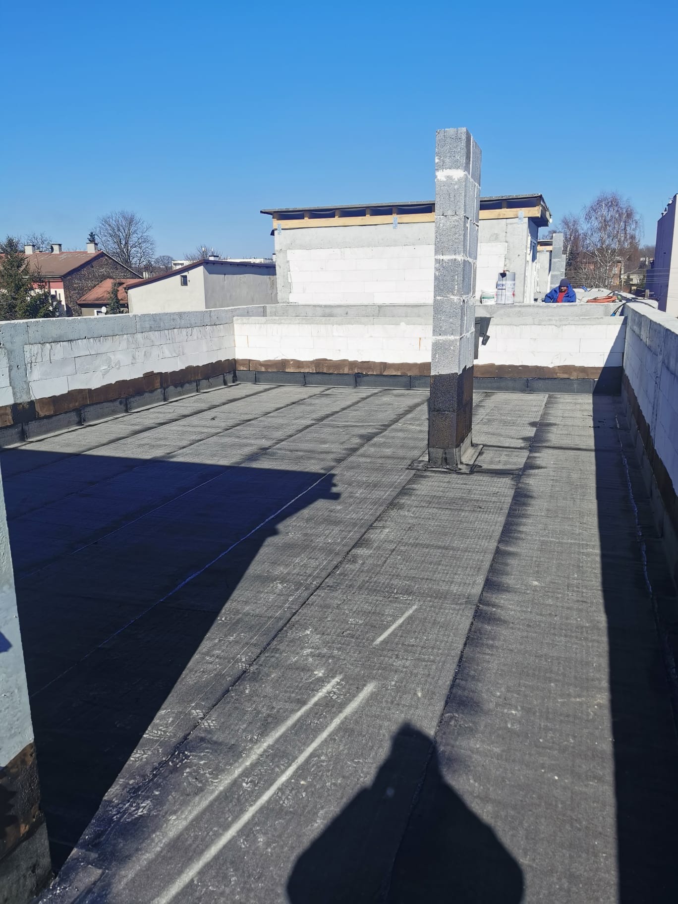 Budowa domu murowanego w Mysłowicach: widok na płaski dach pokryty papą termozgrzewalną, komin z bloczków betonowych w trakcie wznoszenia, ściany z betonu komórkowego.