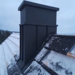 Nowoczesny, grafitowy komin systemowy na dachu pokrytym śniegiem, widok z g&oacute;ry w pochmurny dzień.