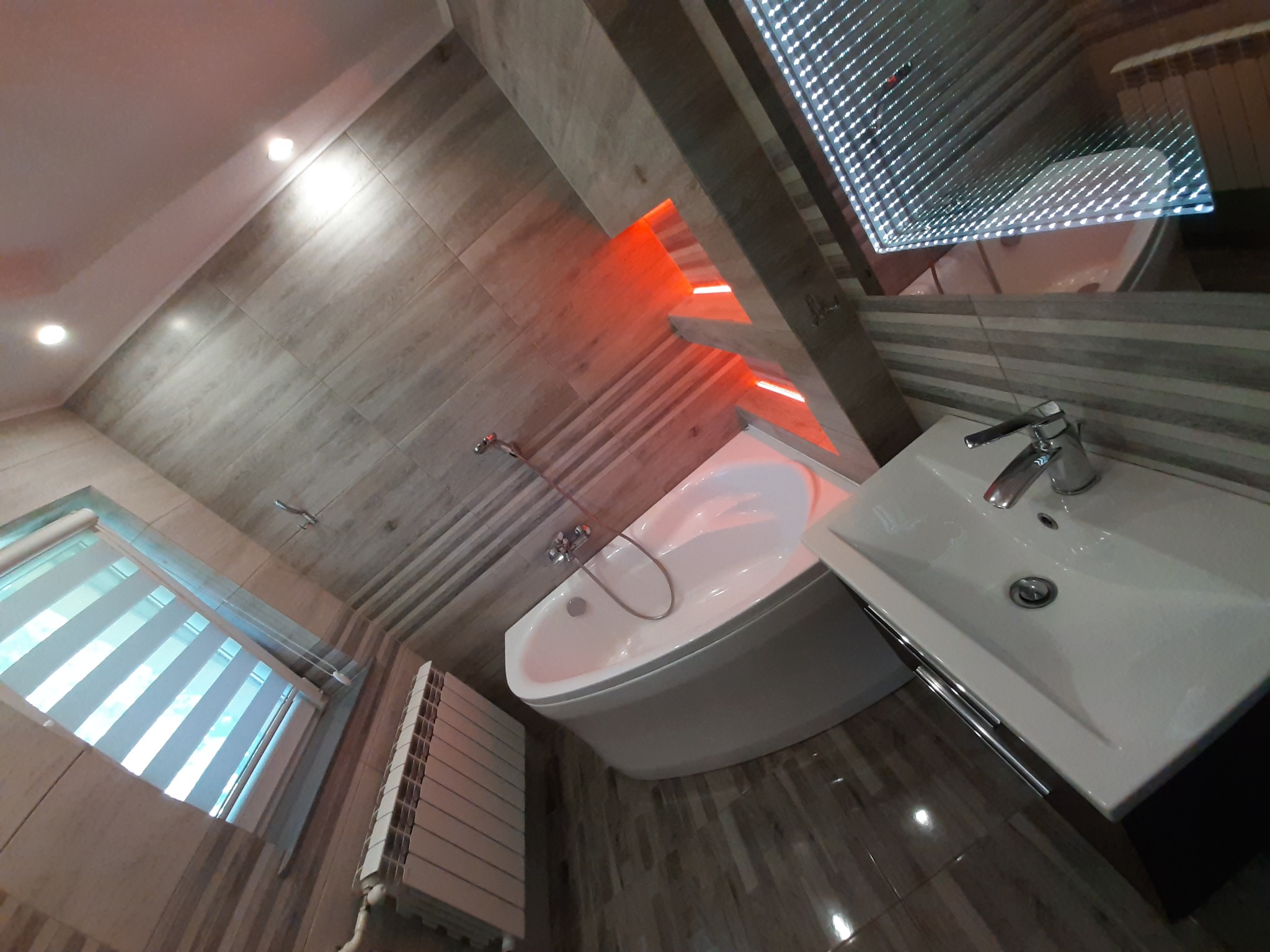 Nowoczesna łazienka z narożną wanną, umywalką nablatową i podświetlanym sufitem LED, widok z góry pod kątem.