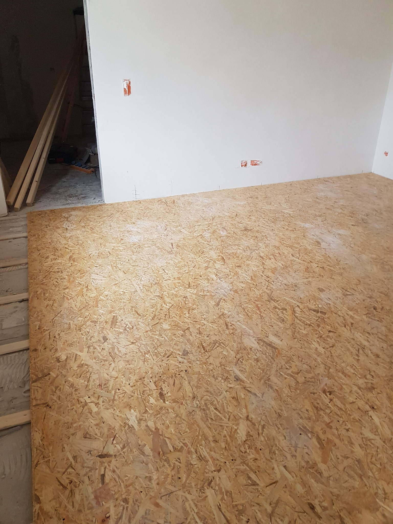 Płyta OSB ułożona na podłodze w trakcie prac wykończeniowych; widoczne ślady po instalacji elektrycznej na ścianie.