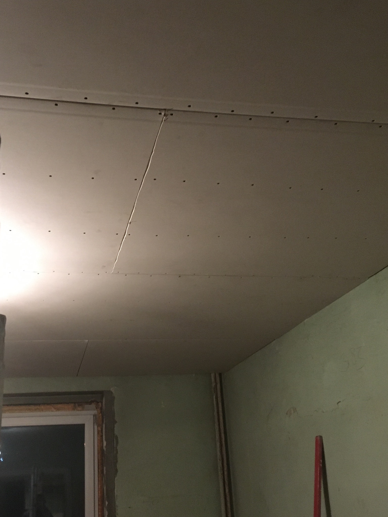 Płyta gipsowo-kartonowa zamontowana na suficie, widoczne łączenia i śruby, ściana pomalowana na zielono, okno w trakcie montażu.