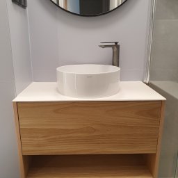 Zakład Stolarski ASKO Joanna Kołodziejska - Nowoczesna łazienka z okrągłą białą umywalką nablatową, armaturą w kolorze grafitowym i szafką z jasnego drewna z otwartą półką, odbicie w okrągłym lustrze.