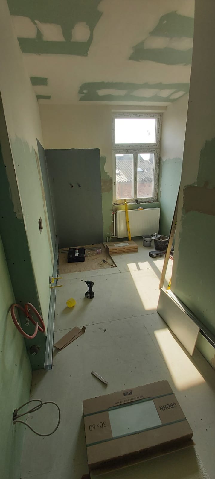 Wnętrze w trakcie prac wykończeniowych: widoczne płyty gipsowo-kartonowe na ścianach i suficie z miejscowymi śladami szpachli, narzędzia pracy takie jak wiertarka akumulatorowa, poziomica,...