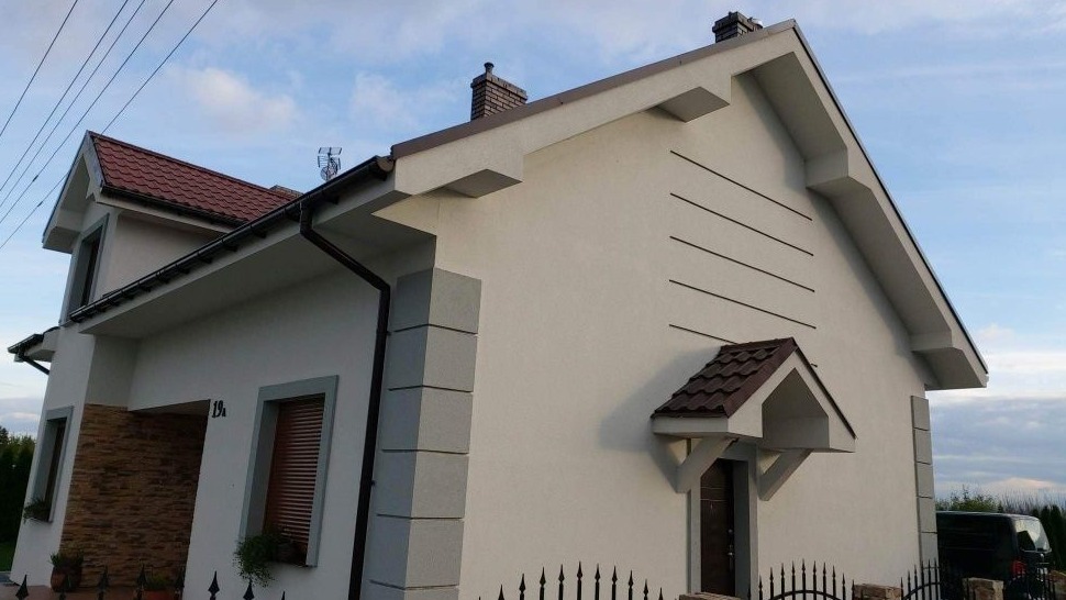 Odnowiona elewacja domu jednorodzinnego z elementami dekoracyjnymi w postaci poziomych linii i kamiennych narożników, widok z niskiej perspektywy.
