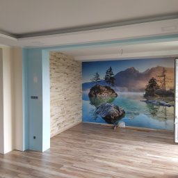Usługi Remontowo-Budowlane ArtBud Dawid Wiśniewski - Wnętrze pokoju po remoncie z panelami podłogowymi, tapetą z motywem górskiego jeziora i ścianą wyłożoną dekoracyjną cegłą.