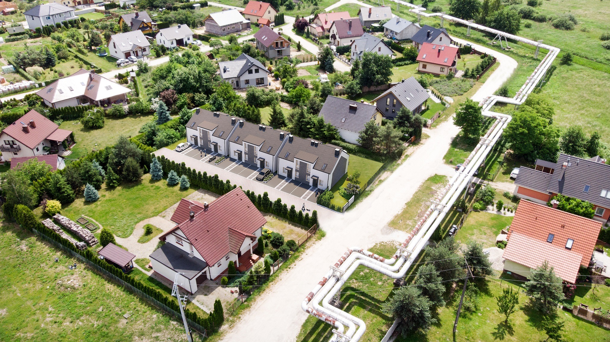 Widok z lotu ptaka na osiedle domów jednorodzinnych, w tym szeregowych, z charakterystycznym przebiegiem rurociągu ciepłowniczego biegnącego wzdłuż drogi.