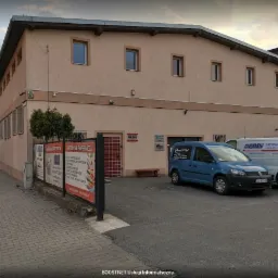 Budynek firmy z zaparkowanymi samochodami dostawczymi, w tym jeden oznaczony logo 'BoostNET Usługi Informatyczne'.