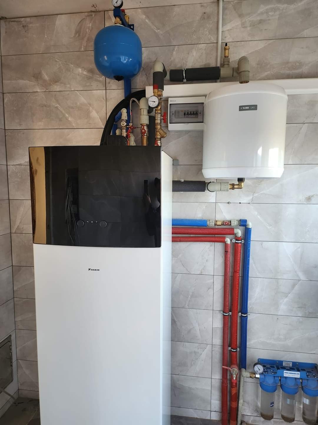 Nowoczesna instalacja grzewcza z pompą ciepła Daikin, zasobnikiem wody Nibe Biawar i filtrami, widoczne rury w kolorze czerwonym i niebieskim, manometry oraz zabezpieczenia