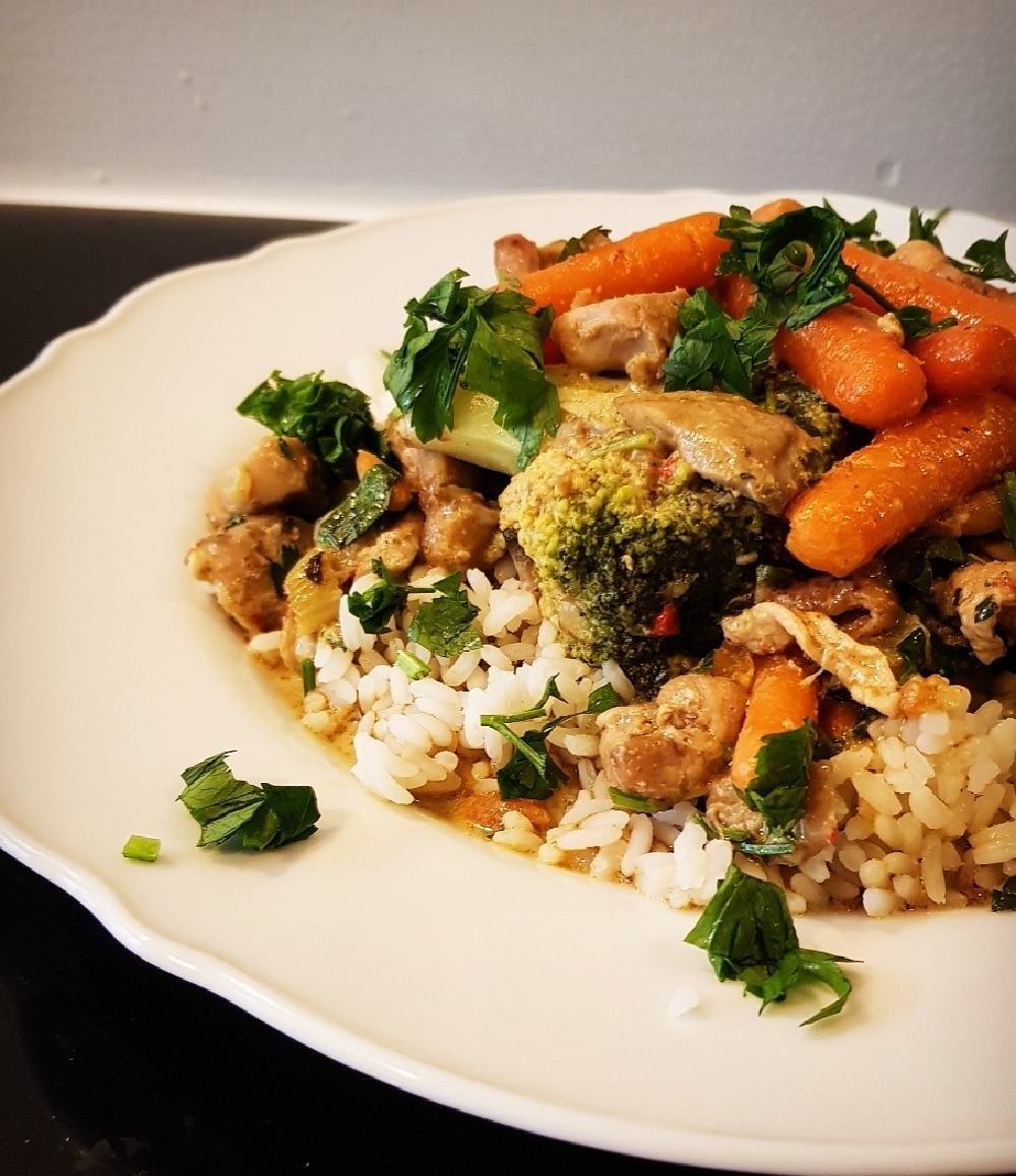 Porcja ryżu z kurczakiem, marchewką, brokułami i zieloną pietruszką na białym talerzu z falistym brzegiem.