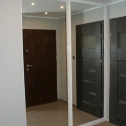 Wnętrze przedpokoju z dużą szafą wnękową z przesuwnymi drzwiami lustrzanymi, widoczne drzwi wejściowe i panele podłogowe.