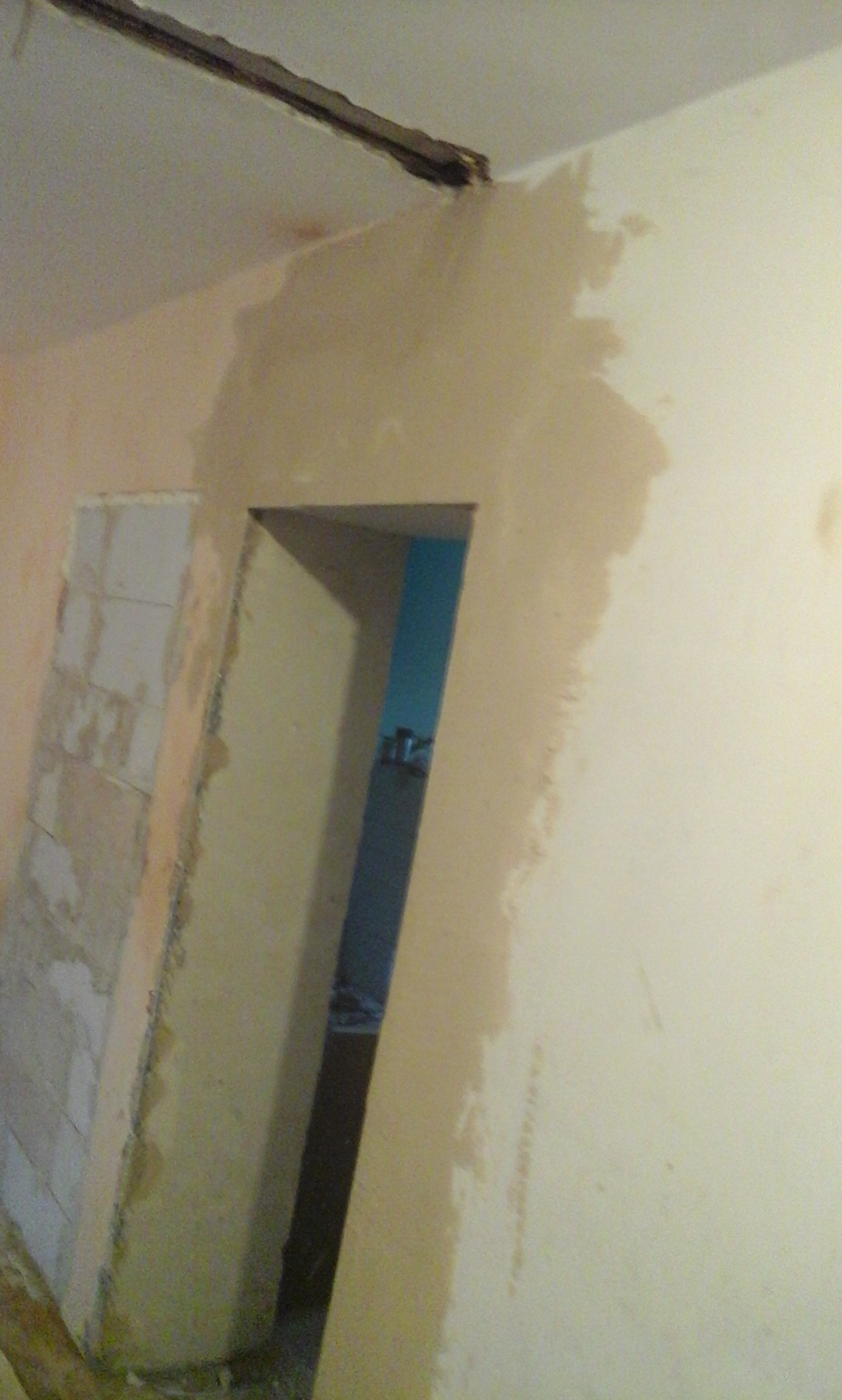 Przygotowanie ściany do malowania: fragment ściany z nałożoną warstwą wyrównującą, widoczne ślady po szpachlowaniu przy futrynie drzwiowej i na suficie.