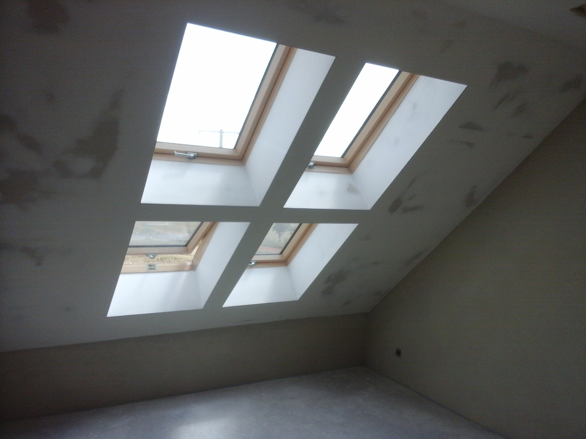 Cztery okna dachowe w skośnym suficie, po szpachlowaniu, przed malowaniem, widoczne ślady po szpachli.