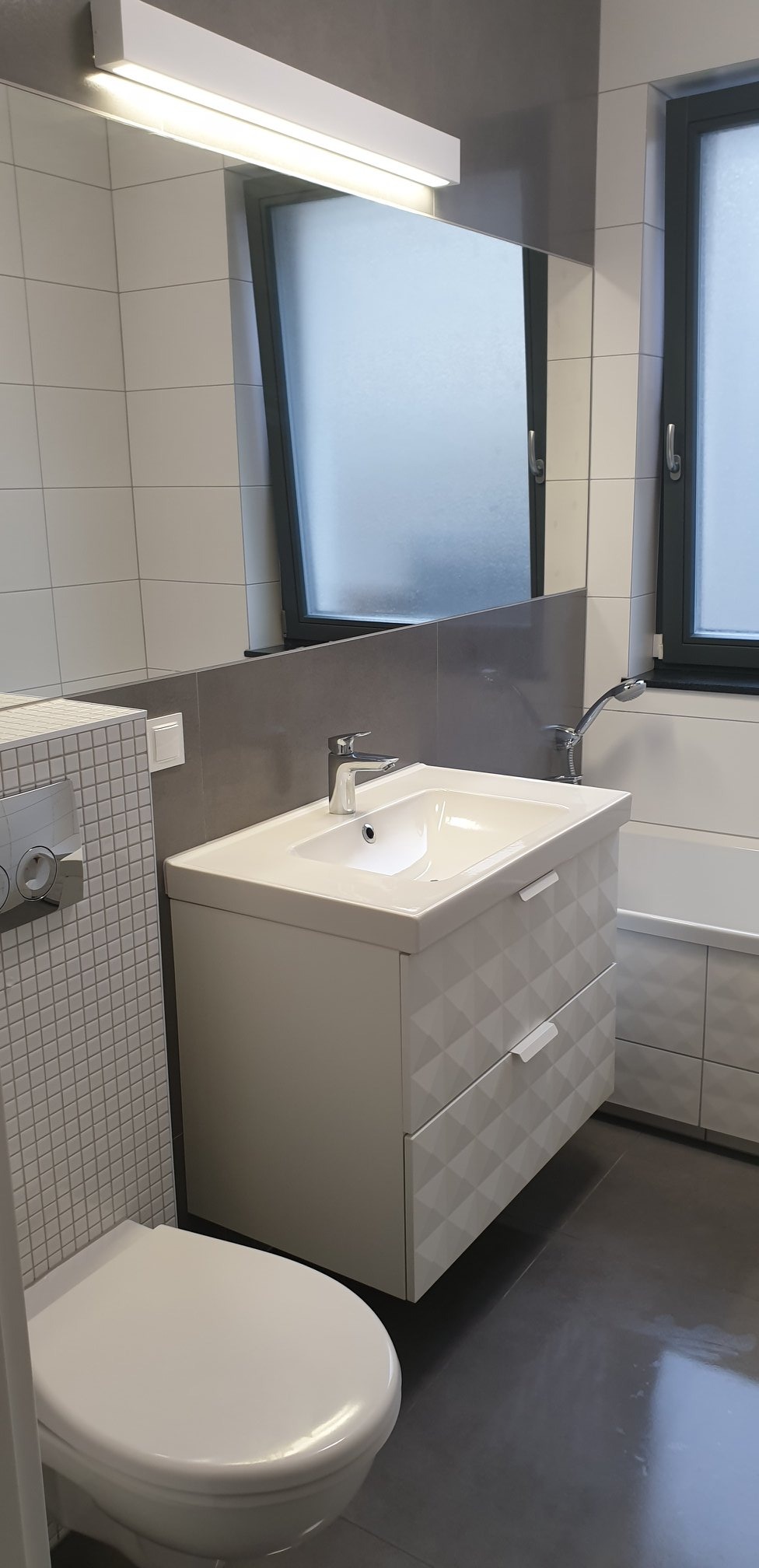 Nowoczesna łazienka z białymi płytkami, szafką pod umywalkę z geometrycznym wzorem i podwieszaną toaletą.