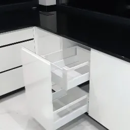 Wysuwana, dwupoziomowa szuflada cargo w białej, nowoczesnej zabudowie kuchennej z czarnym blatem, widok na marmurową podłogę.