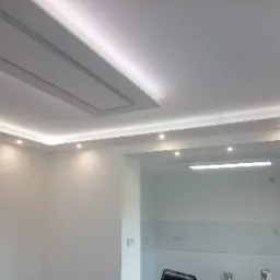 Biały sufit podwieszany z oświetleniem LED, w tym centralny panel z ukrytą klapą dostępową i punktowe lampy halogenowe.