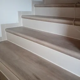 Schody wykończone panelami imitującymi drewno, z białymi listwami przypodłogowymi i zaokrąglonymi krawędziami stopni, widok z dołu.