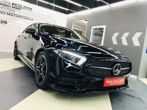 Błyszczący, czarny Mercedes-Benz CLS z charakterystycznym grillem i logo, zaparkowany w salonie z napisem 'SPA POSEJDON' na ścianie.