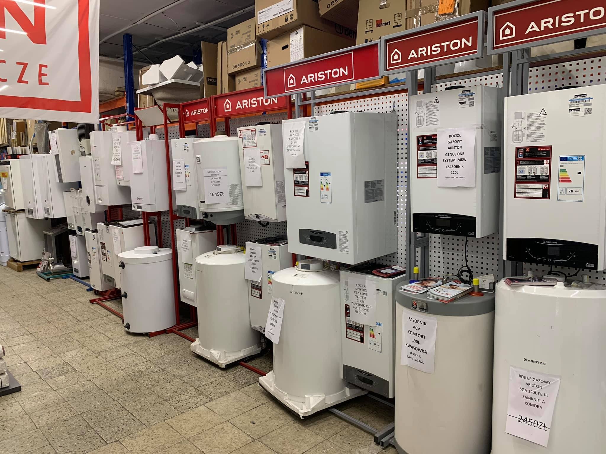 Rząd kotłów gazowych i zasobników ciepłej wody marki Ariston, wystawionych w sklepie budowlanym, z widocznymi cenami i specyfikacjami na etykietach.