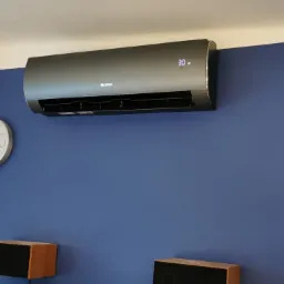 Czarny klimatyzator Gree zamontowany na niebieskiej ścianie w mieszkaniu w Orzeszu, obok biały zegar i półka z książkami.