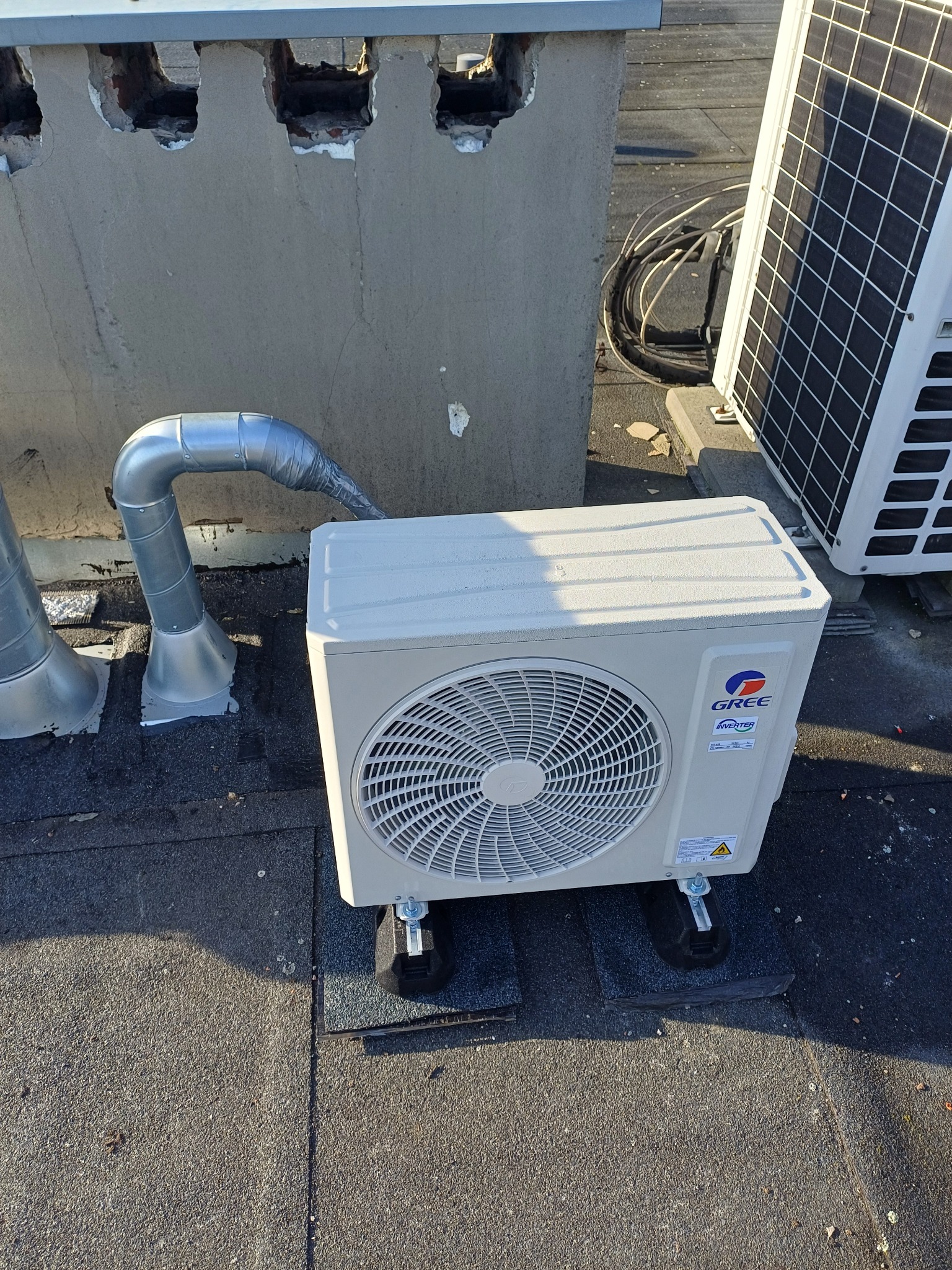 Jednostka zewnętrzna klimatyzacji marki Gree zamontowana na dachu, widoczne przewody i elementy mocujące.