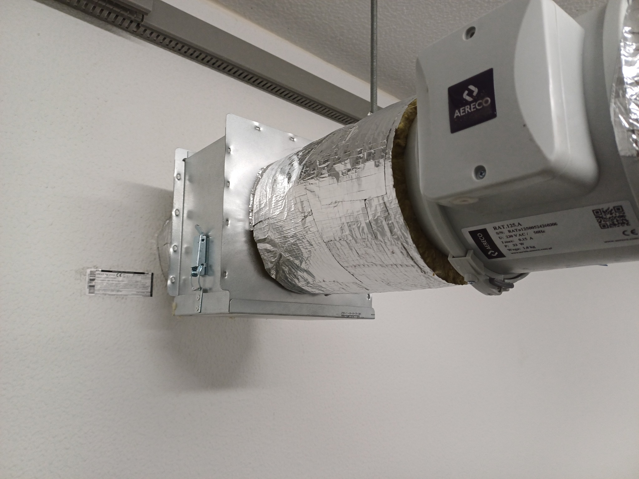 Szczegół montażu rekuperatora AERECO z izolacją termiczną, widoczny element mocujący do ściany i zawieszenie na lince stalowej.