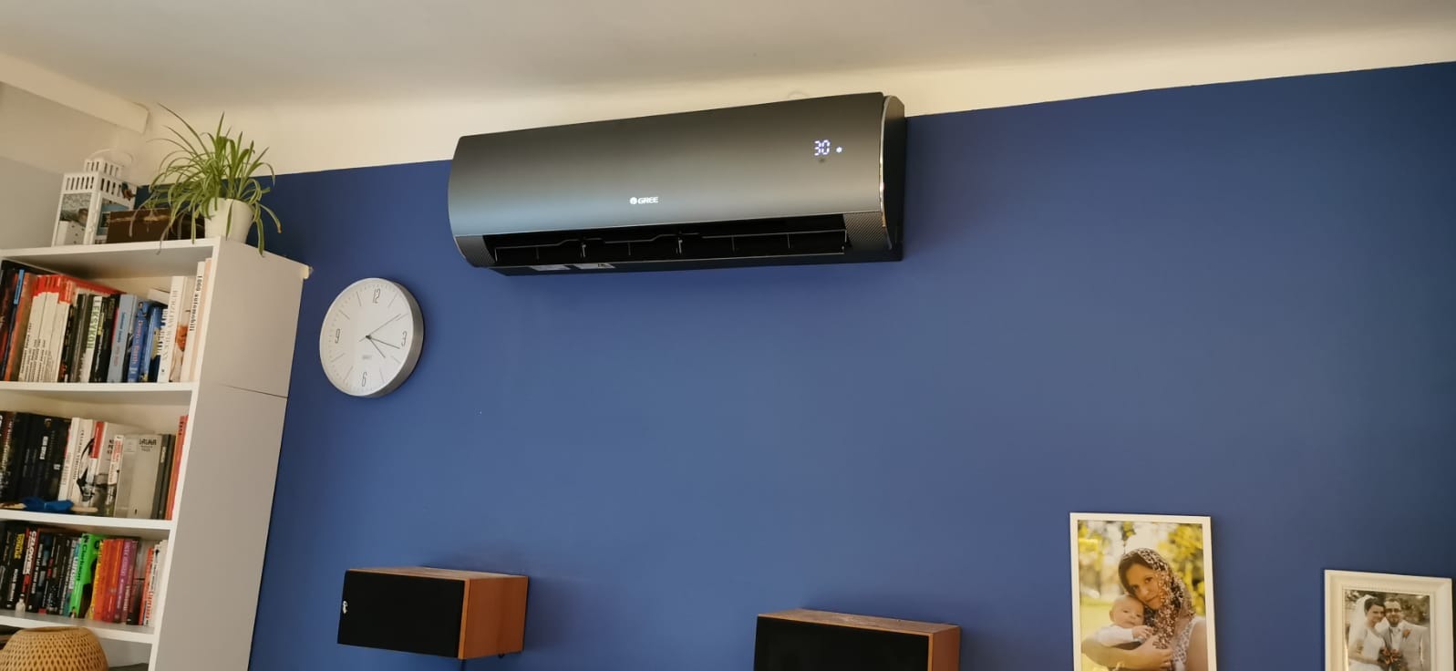Czarny klimatyzator Gree zamontowany na niebieskiej ścianie w mieszkaniu w Orzeszu, obok biały zegar i półka z książkami.