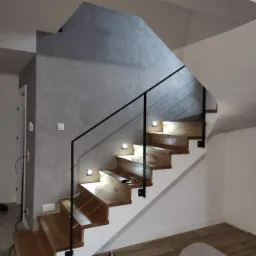 Nowoczesne schody z drewnianymi stopniami, oświetleniem LED i czarną balustradą z linkami, widok z dołu