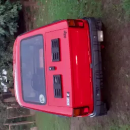 Czerwony Fiat 126p (Maluch) z tyłu, z polską tablicą rejestracyjną, zaparkowany na zewnątrz na tle zieleni.