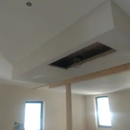 Wnętrze w trakcie remontu: widoczna konstrukcja z płyty kartonowo-gipsowej na suficie z otworem, wsparta drewnianymi stemplami, drabina oparta o ścianę przy oknie.