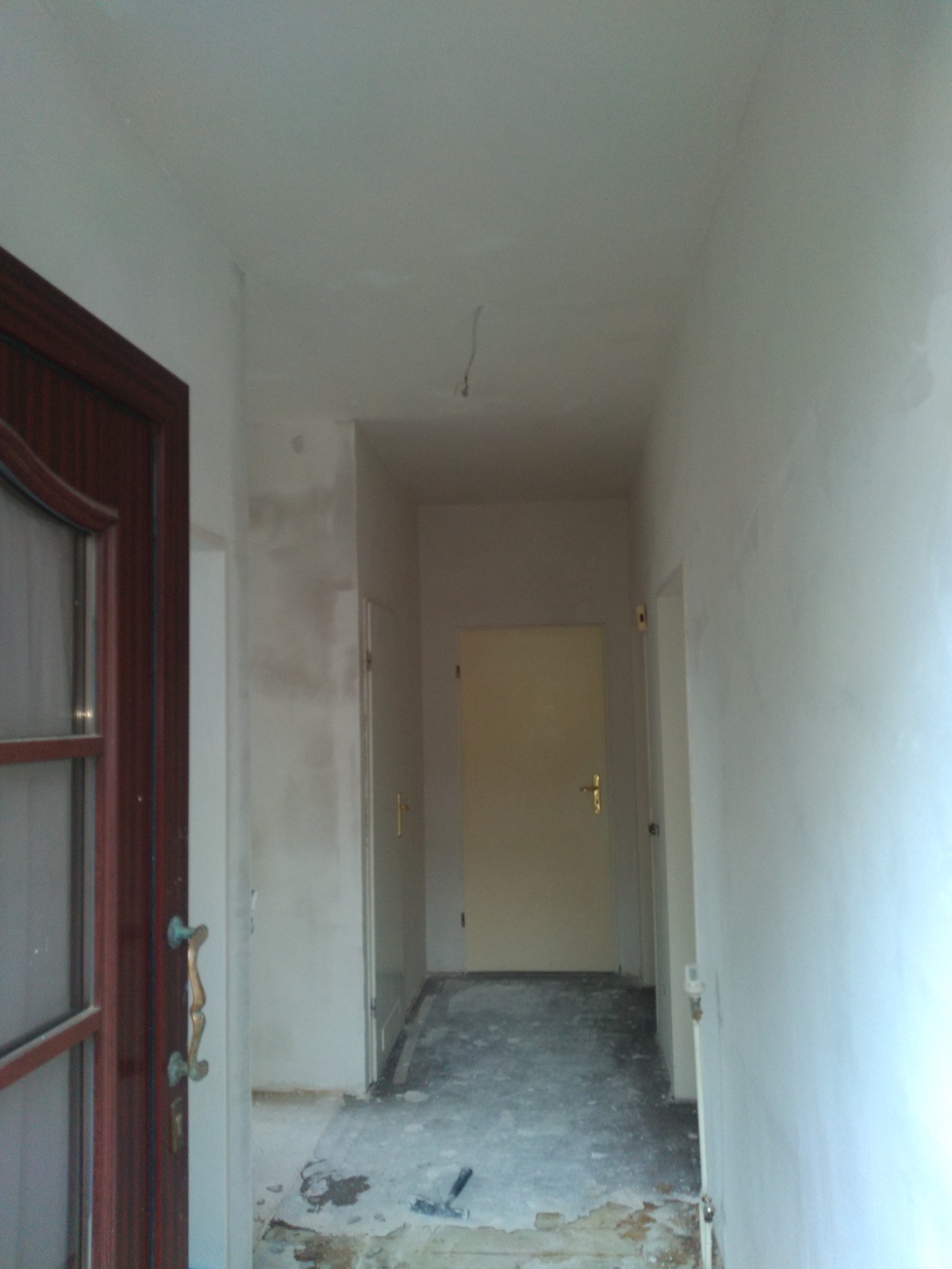 Korytarz w trakcie remontu: ściany po szpachlowaniu, częściowo zagruntowane, widoczne ślady po remoncie na podłodze, stara stolarka drzwiowa.