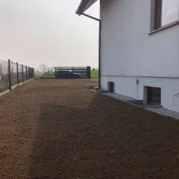 Przygotowany teren pod trawnik w Spytkowicach, widoczny świeżo wyrównany grunt, ogrodzenie panelowe i fragment elewacji budynku.