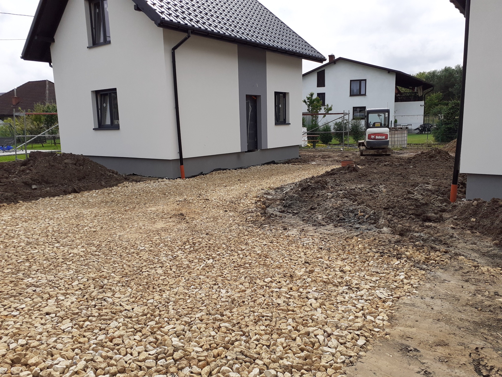 Żwirowa droga dojazdowa do nowo wybudowanego domu, z mini koparką Bobcat w tle, przygotowana pod dalsze prace.