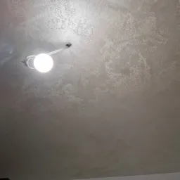 Szara, teksturowana powierzchnia sufitu z widoczną żarówką i elementami wentylacji.