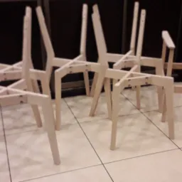 Szkielety drewnianych krzeseł w trakcie montażu, widoczne elementy konstrukcyjne i łączenia śrubowe.