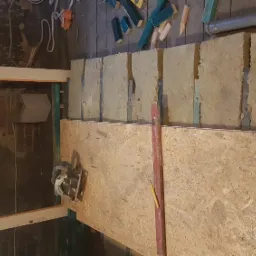 Wnętrze w trakcie prac wykończeniowych: izolacja ścian wełną mineralną, płyta OSB, poziomica, narzędzia i materiały budowlane w tle.