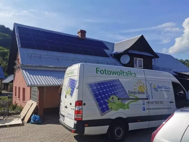 Instalacja paneli słonecznych na dachu domu jednorodzinnego, widoczny firmowy bus z logo i danymi kontaktowymi wykonawcy.